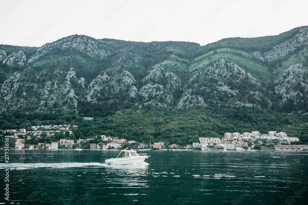 Beautiful view of the natural landscape, the sea and the coastal city near the mountains in Montenegro. Boat sailing on the sea.