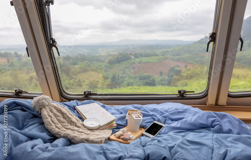 A cup of hot coffee with marshmallow near the window in the caravan camping car in the rain season,travel camping concept.