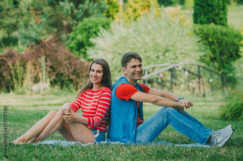 Young couple in love is sitting on the plaid in the park, back to back and enjoying the nature. Picnic for couples in love.