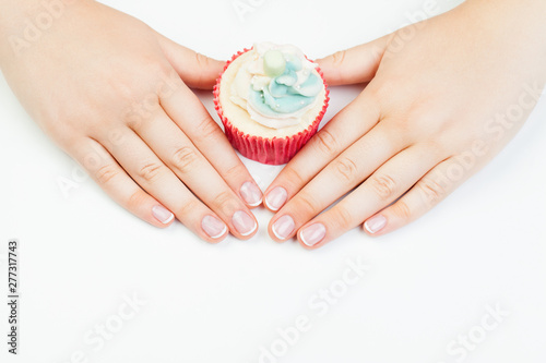 Woman hands with french manicured nails holding cupcake on white background
