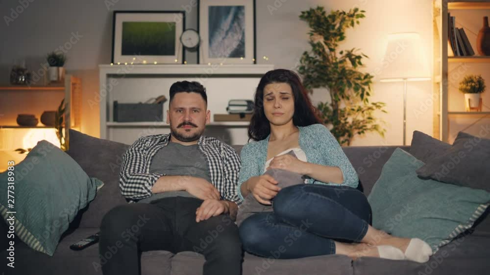 Young people girl and guy are watching sad movie on TV crying sitting on couch in apartment together concentrated on television. Leisure and emotions concept. Young people girl and guy are watching sad movie on TV crying sitting on couch in apartment together concentrated on television. Leisure and emotions concept.