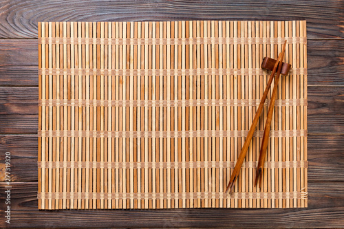 two sushi chopsticks with empty brown bamboo mat or wood plate on wooden Background Top view with copy space. empty asian food background photo