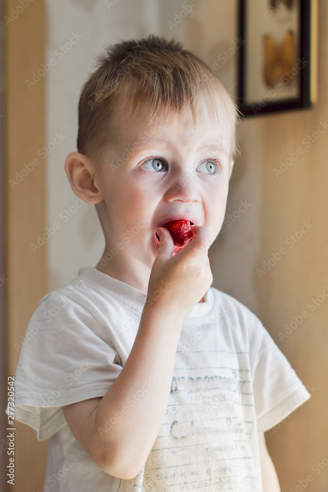 a boy of three years in a Sunny kitchen eating ripe red strawberries a boy of three years in a Sunny kitchen eating ripe red strawberries