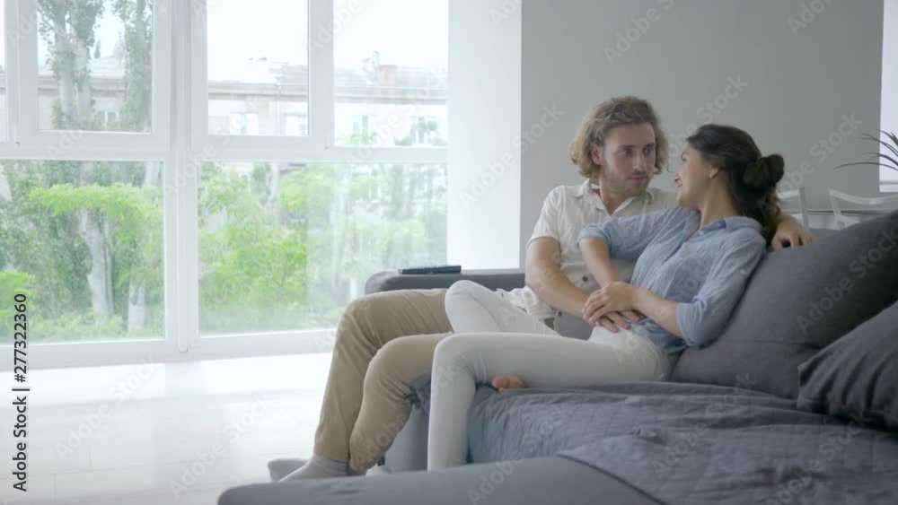 happy pregnant, young female with excitement tells male about pregnancy and puts hands on belly and future parent smiles happily sitting on couch at home