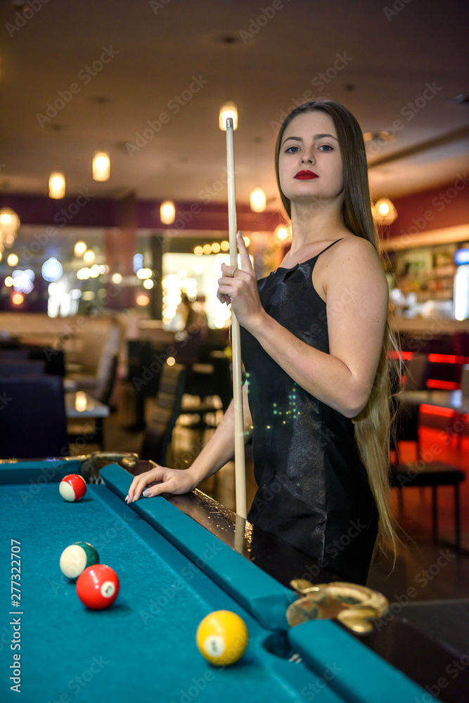 Fototapeta premium Woman with cue posing in billiard pub