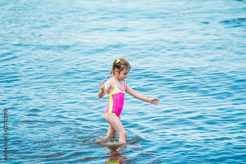 Little girl in a swimsuit and striped bathing in the sea in summer, making a splash and running in water