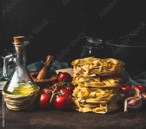 Quadro em tela Italian pasta with tomatoes, olives oil and garlic on dark rustic kitchen counter at dark background