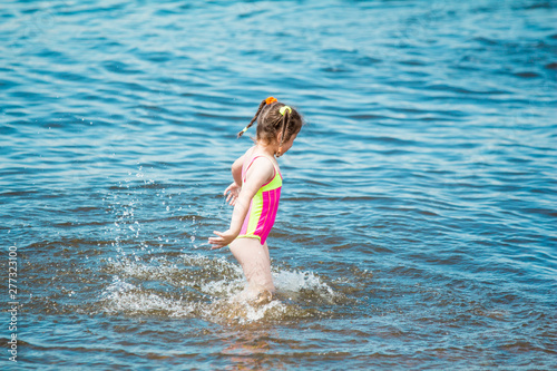 Little girl in a swimsuit and striped bathing in the sea in summer, making a splash and running in water © kapichka
