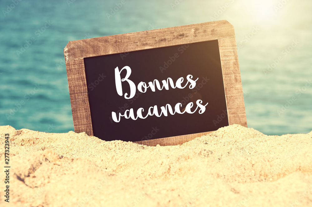 Bonnes vacances (meaning Happy holiday in French) written on a vintage chalkboard in the sand of a beach - obrazy, fototapety, plakaty 