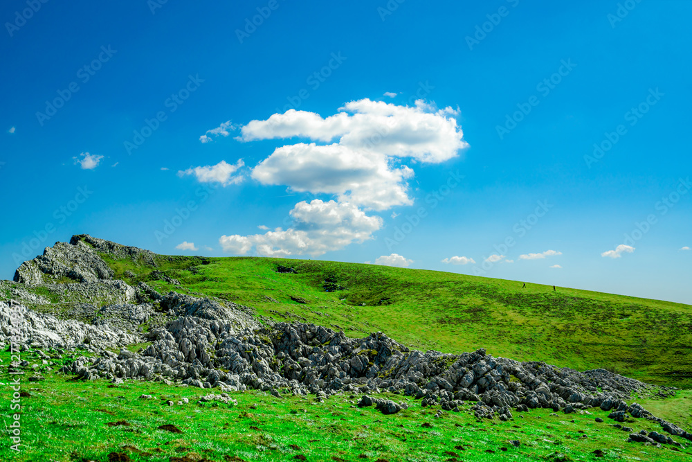 Landscape of green grass and rock hill in spring with beautiful blue sky and white clouds. Countryside or rural view. Nature background in sunny day. Fresh air environment. Stone on the mountain.
