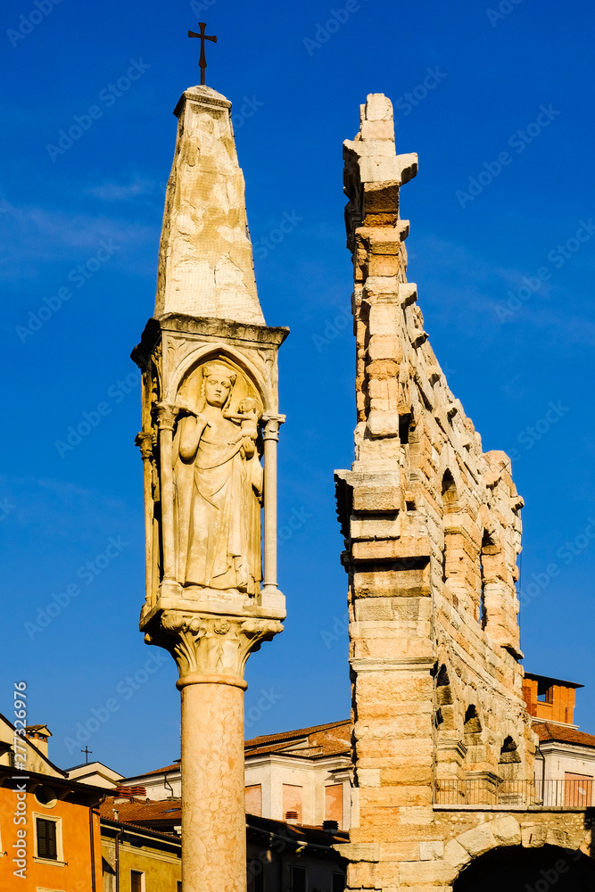 Verona, Italy: Medieval Column with the Virgin and ruins of the outer wall of the Roman amphitheater. Closeup view.