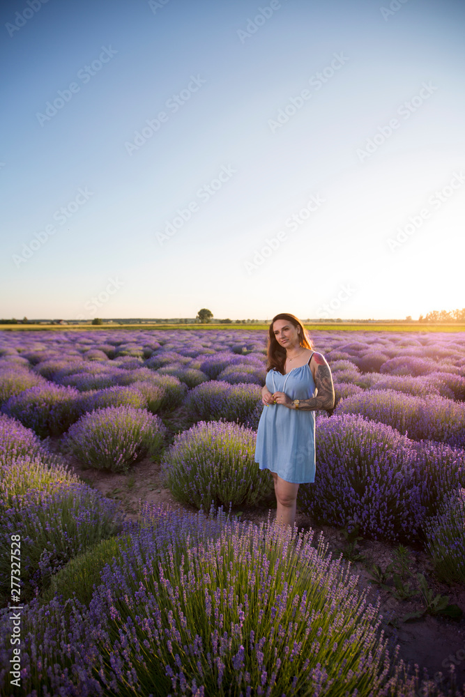 Young, beautiful, pretty girl with tattoos in a dress. Woman standing among blooming colorful flowers in a lavender field during a warm summer sunset. Young, beautiful, pretty girl with tattoos in a dress. Woman standing among blooming colorful flowers in a lavender field during a warm summer sunset.
