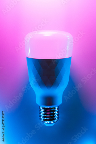 Smart Home RGB bulb lamp in trendy backlight. LED Bulb, multicolor backdrop inspired by neon trend. Top view, copy space for your design
