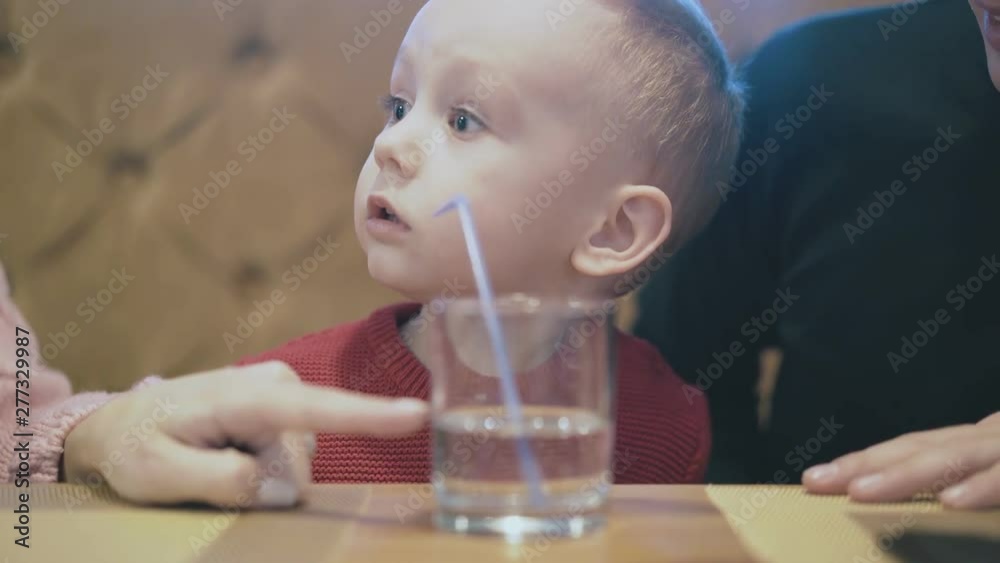 parents show child in red pullover glass with water and plastic straw on table pointing with fingers extreme close view parents show child in red pullover glass with water and plastic straw on table pointing with fingers extreme close view