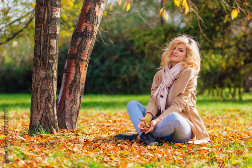 Young beautiful woman sitting on the ground coverd with fallen autumn leaves