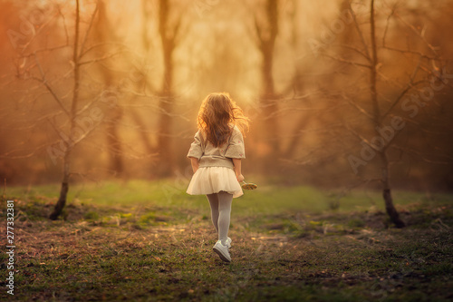 back view of small girl standing in the spring park between the trees