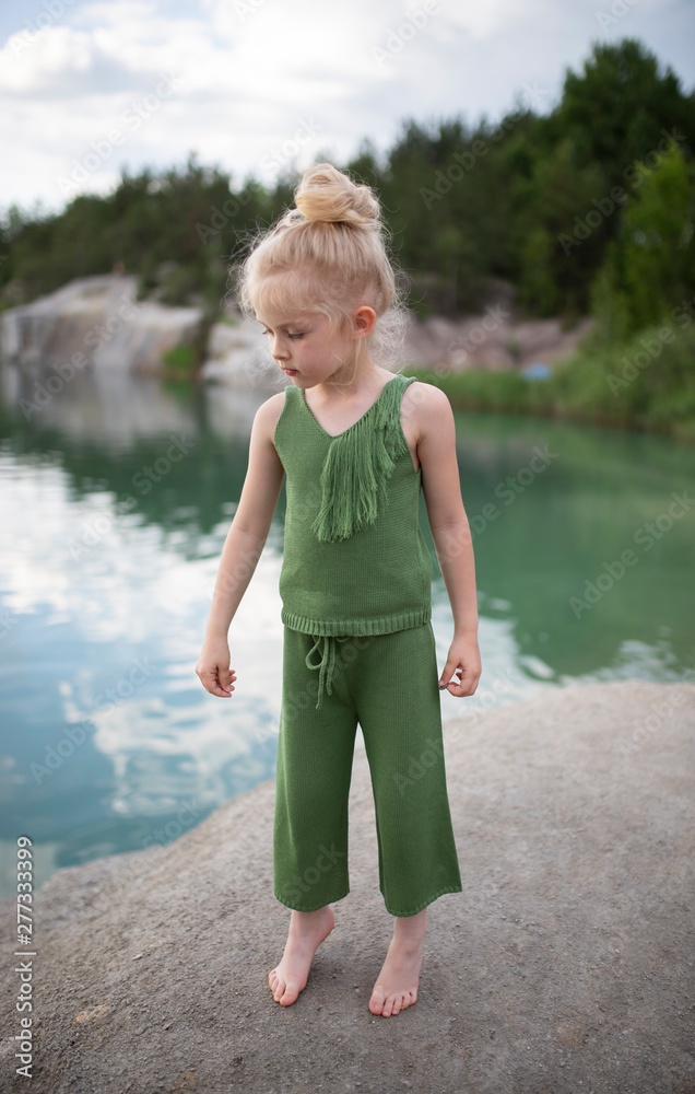 Little cute girl in stylish clothes on a background of rocks. Summer portrait of a little girl cotton clothes for a magazine or advertisement Little cute girl in stylish clothes on a background of rocks. Summer portrait of a little girl cotton clothes for a magazine or advertisement