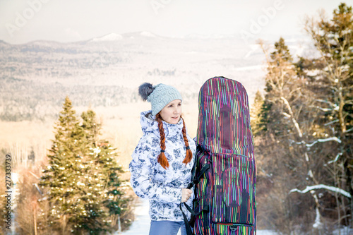 Girl snowboarder standing on a ski track, holding a case with her snowboard and enjoying the ski resort