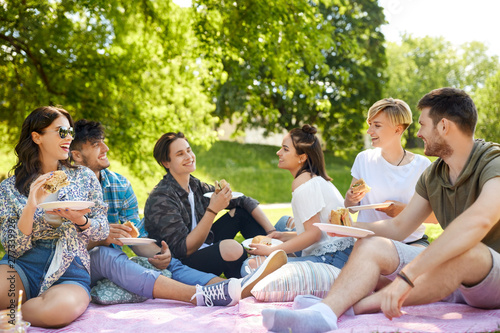 friendship  leisure and fast food concept - group of happy friends eating sandwiches or burgers at picnic in summer park