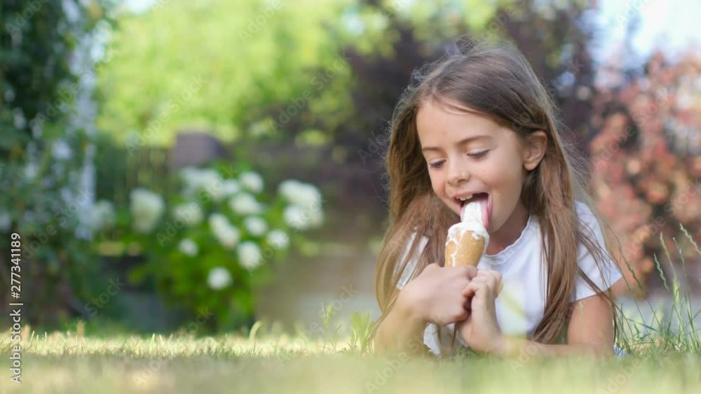 Beautiful little girl with a tasty ice cream lies on the lawn in the park and enjoys. Child with ice cream on the lawn. 4K UHD Beautiful little girl with a tasty ice cream lies on the lawn in the park and enjoys. Child with ice cream on the lawn. 4K UHD