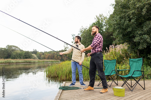 leisure and people concept - male friends with fishing rods on lake pier