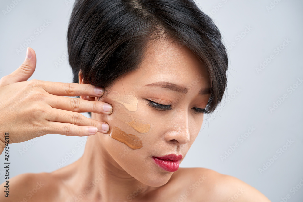 Close-up of beautiful Asian woman with short dark hair making make-up and applying three different tones of foundation on her face