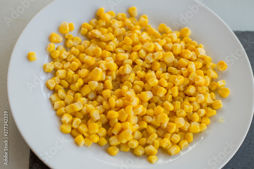 Pile of yellow corn grains with spoon on white plate, close-up