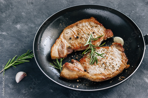 Roasted pork steaks in a frying pan with rosemary and garlic close up.