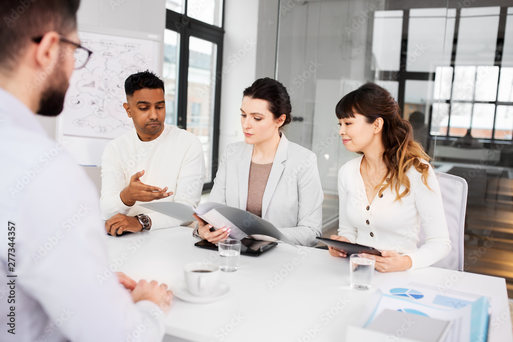 new job, hiring and employment concept - international team of recruiters with tablet computer and folder having interview with male employee at office