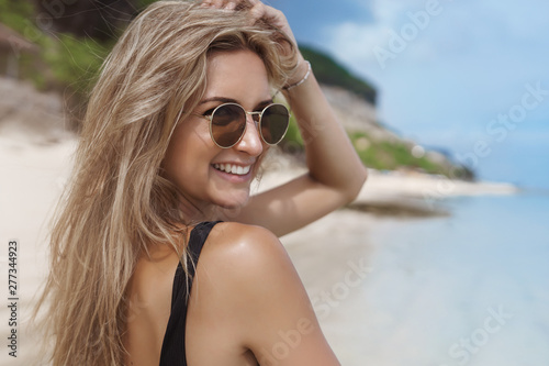 Close-up happy carefree woman walking sandy beach near ocean turn behind smile camera touch hair wear sunglasses enjoy awesome summer vacation, wanna swim, like seaside view, travelling © Liubov Levytska