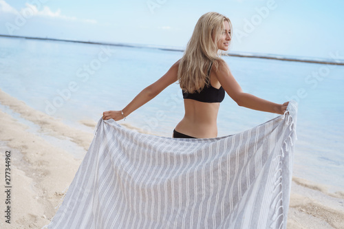 Back biew charming romantic blond woman feel relieved relaxed, look carefree contemplating blue ocean hold blanket towel wanna lie down sandy beach sunbathing enjoy summer vacation travel photo