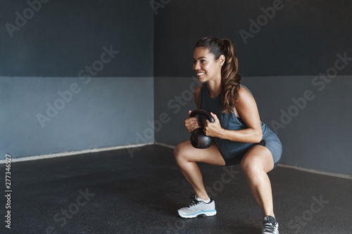 Girl prepare body good shape, lead active lifestyle, determined gain strong muscles, Sportswoman perform squats exercise, lift kettlebell smiling motivated, training session alone gym workout