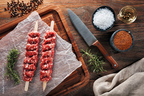 Raw Turkish Urfa kebab on white cooking paper and wooden cutting table. Dercorated with herbs, spices and chef's knife. photo