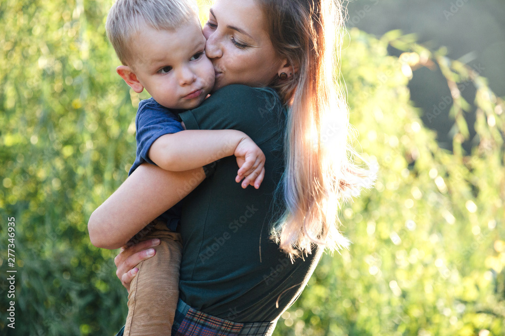 Front view mother and baby son hugging on the road on lake in summer evening time on the shurb background Front view mother and baby son hugging on the road on lake in summer evening time on the shurb background
