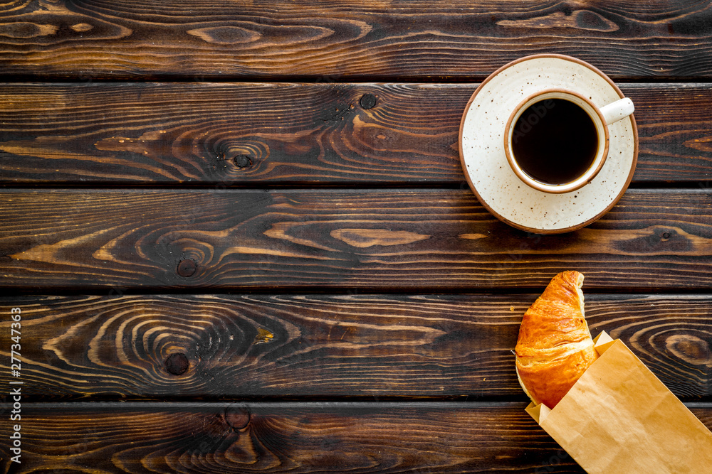 Fototapeta Breakfast with croissant in paper bag and cup of coffee on wooden background top view mock up