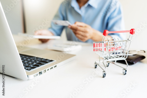 Man holding credit card in hand and entering security code using smart phone on laptop keyboard, online payment shopping concept