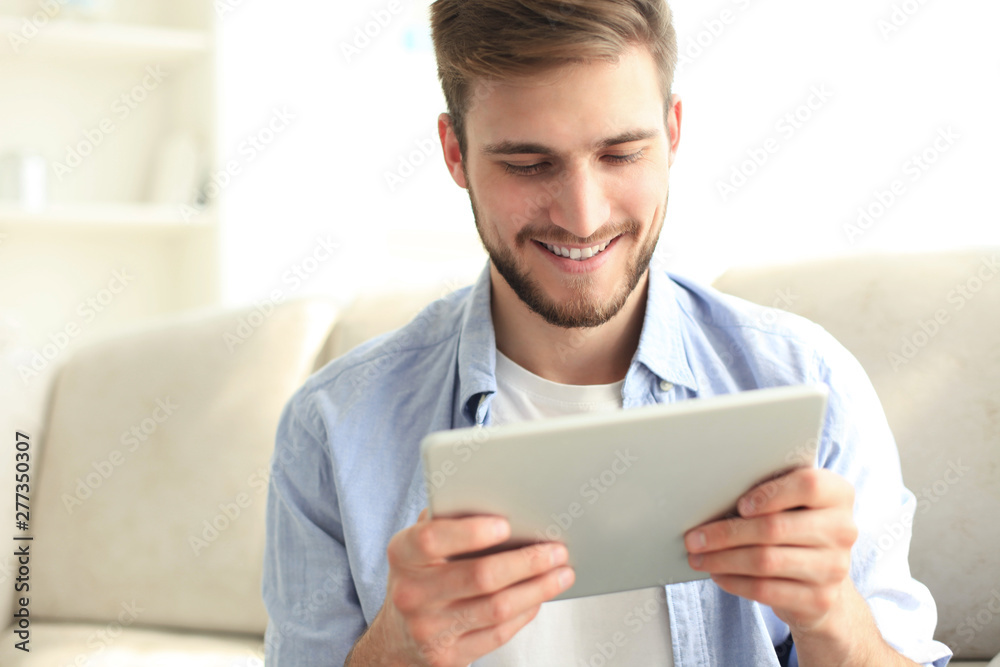 Handsome man is using a digital tablet and smiling while resting on couch at home. Handsome man is using a digital tablet and smiling while resting on couch at home.