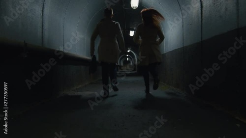 Rear view shot of man and woman in coats with cases running through the illuminated tunnel photo