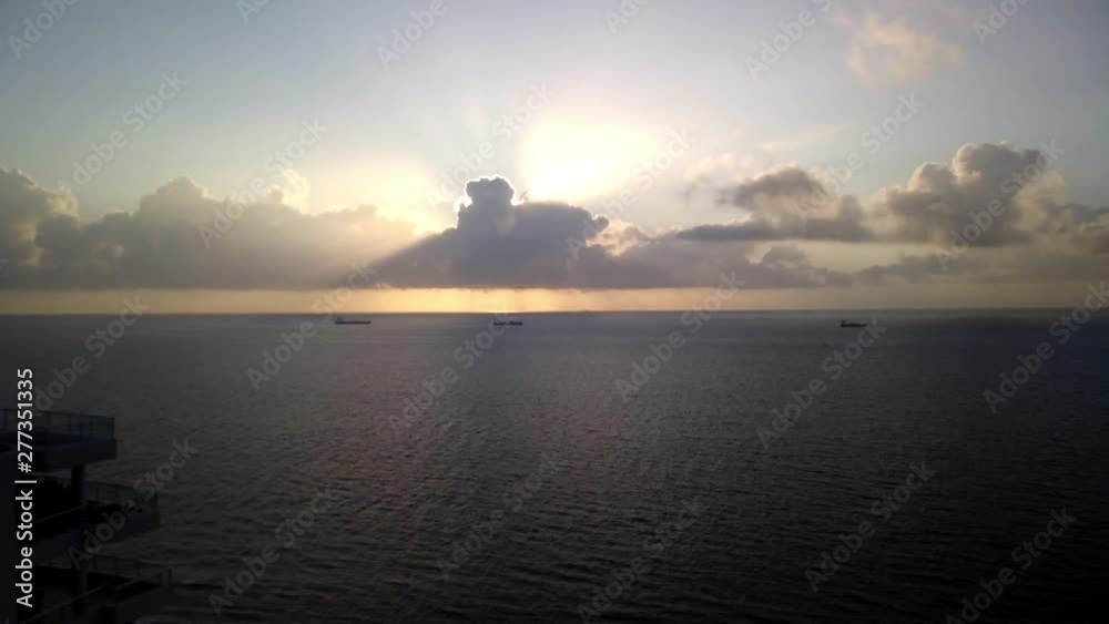 Time lapse of a sunrise over the ocean. Clouds are seen gliding by and a yellow sun ball rises and goes in and out of the clouds. There are three tanker ships on the smooth ocean Time lapse of a sunrise over the ocean. Clouds are seen gliding by and a yellow sun ball rises and goes in and out of the clouds. There are three tanker ships on the smooth ocean