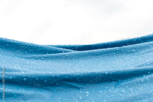 Water drops on the blue nylon fabric tent after rain with white background and copy space.