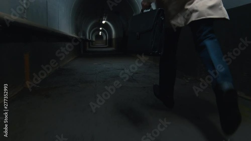 Low-section shot of man in coat with case running in the dark tunnel photo