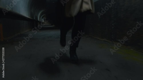 Low-section shot of woman in coat with case starting to run in the dark tunnel photo