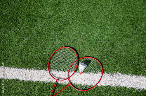 Red badminton rackets and shuttlecock lie on the artificial grass of a sports stadium. Amateur badminton set. Concept of summer hobby, outdoor sports, entertainment. Place for text, flat lay.
