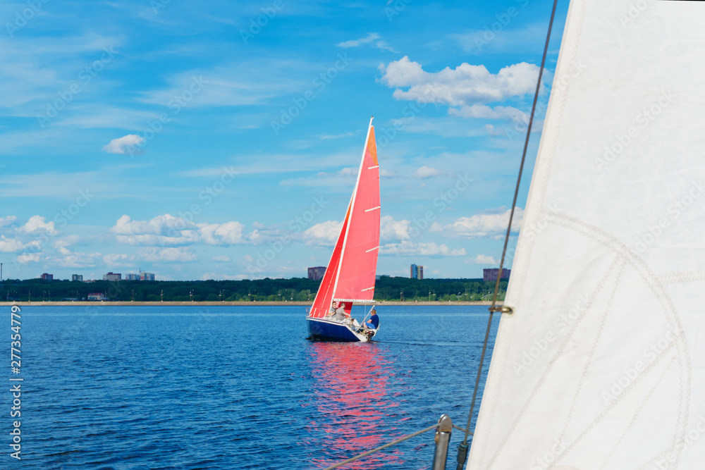 Naklejka premium sailboat with red sails on the background of the shore with an urban landscape