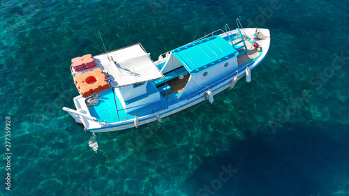 Aerial drone top view photo of traditional colourful fishing boat near iconic beach of Ornos with emerald clear sea, Mykonos island, Cyclades, Greece