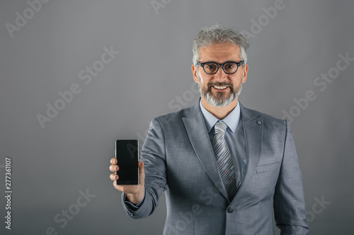 senior businessman showing cellphone on gray background © cherryandbees