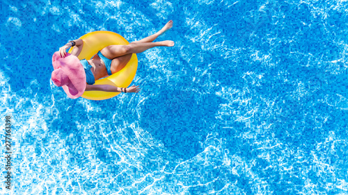 Beautiful young woman in hat in swimming pool aerial top view from above, girl in bikini relaxes and swims on inflatable ring donut and has fun in water on family vacation, tropical holiday resort