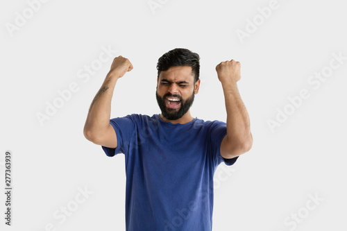 Beautiful male half-length portrait isolated on white studio background. Young emotional hindu man in blue shirt. Facial expression, human emotions, advertising concept. Celebrating like a winner.