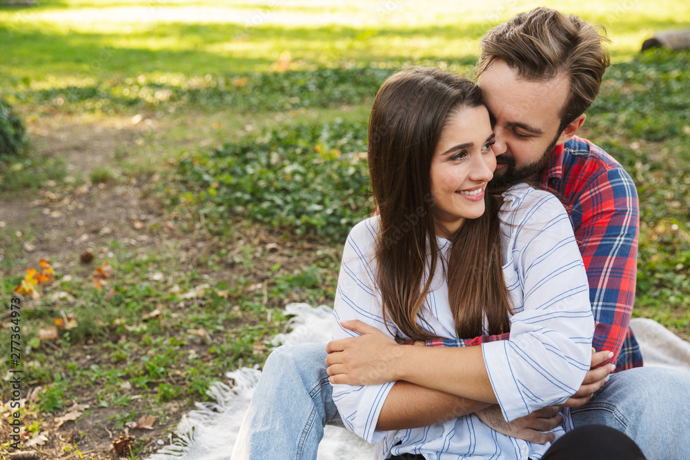Image of lovely couple man and woman hugging while resting in green park