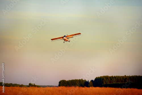 A small plane flying in the sky over the fields and forests. Processing farm fields.